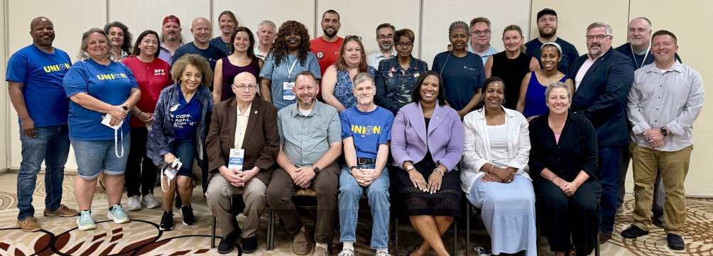 The newly-elected 2025-2027 Executive Council is photographed, with five people seated in the front and the rest standing behind them. They are in front of a beige wall with a tan carpet featuring a circular design with lighter tan and dark brown colors.